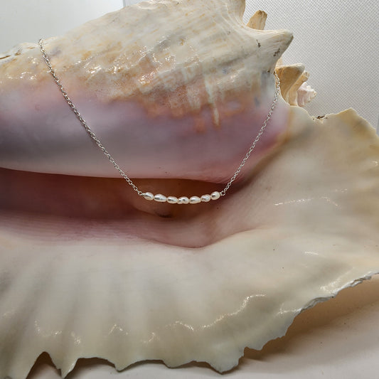 A sterling silver necklace with a bar-shaped freshwater pearl pendant, displayed on a conch shell.